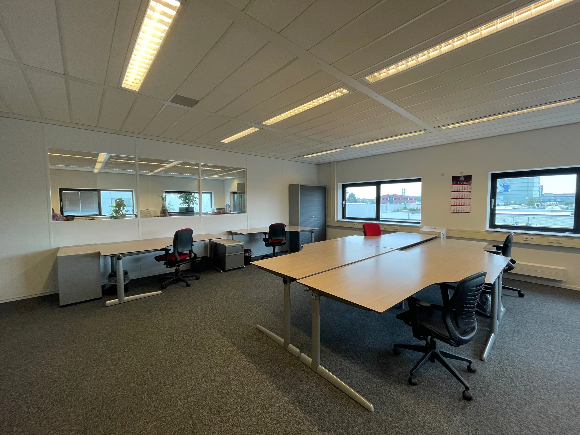 Moderne, ruime kantoorruimte aan de Karel Doormanweg met meerdere bureaus, bureaustoelen en grote ramen met uitzicht op kantoorgebouwen.